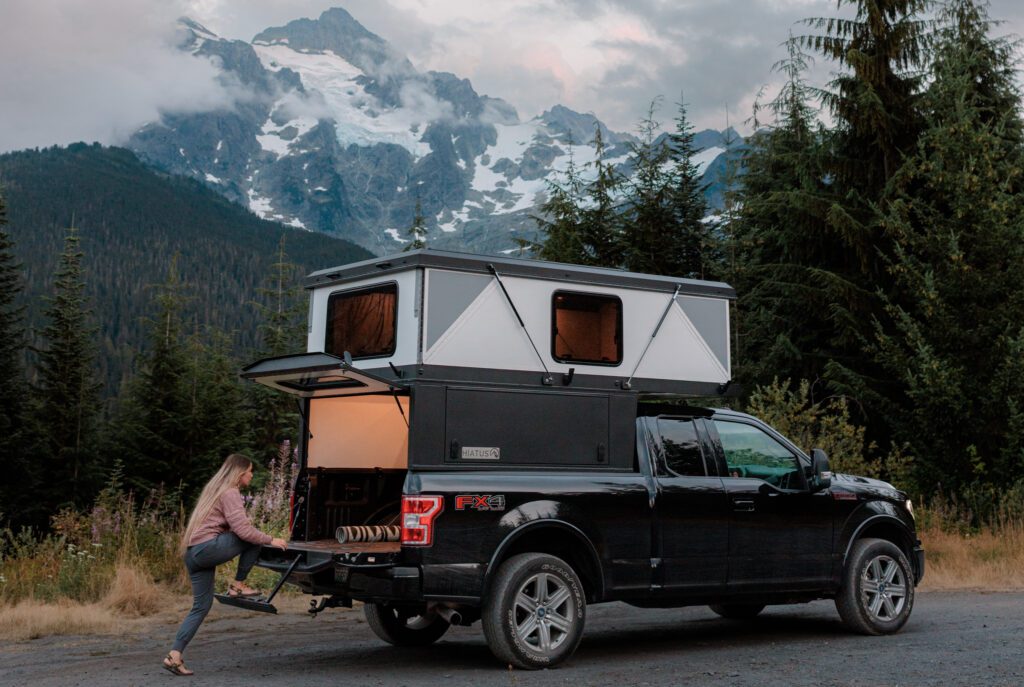 Stepping into a truck camper using a tailgate door on a Ford F-150 with a Hiatus hard-sided pop-up camper in a mountain setting